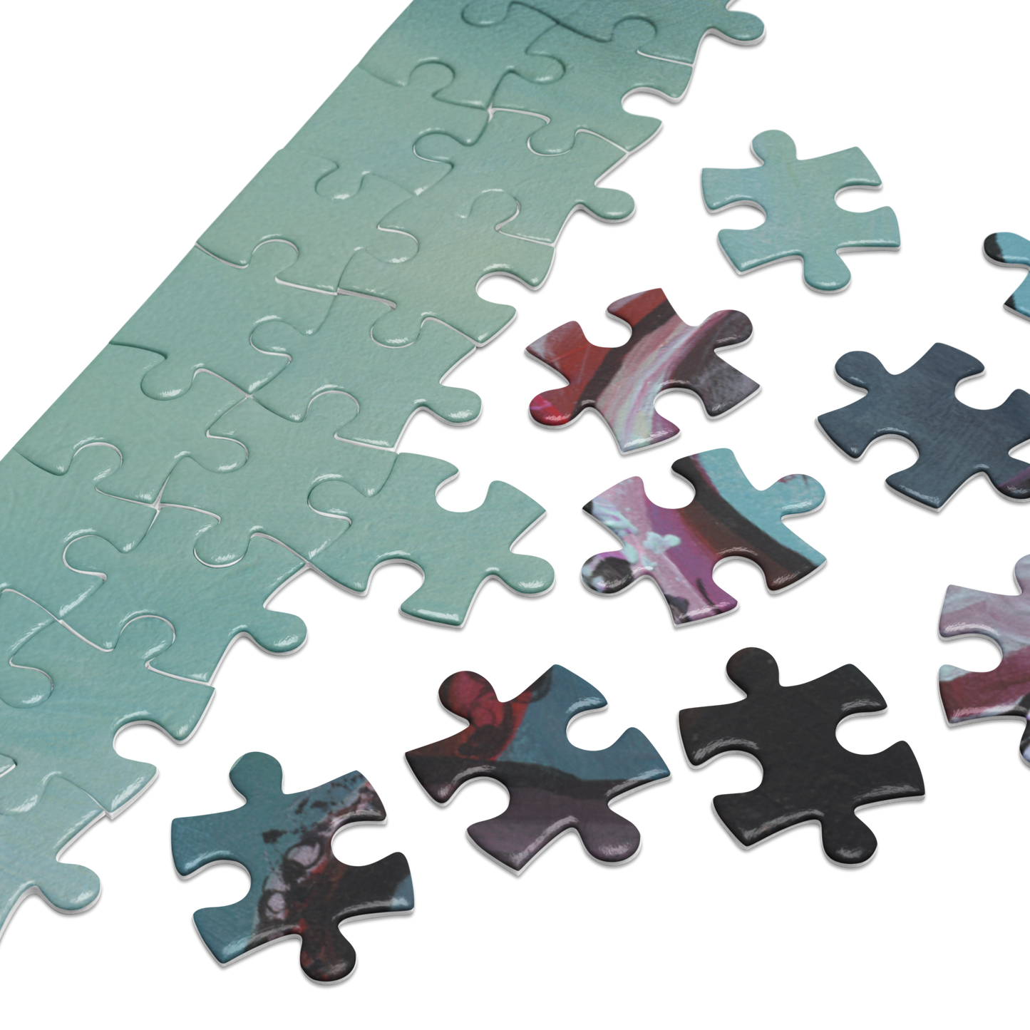 A close-up of a jigsaw puzzle showing a long strip of completed pieces in a pale mint green color, with several loose puzzle pieces beside it featuring a marbled abstract pattern in teal, pink, purple, black, and red on a white background.
