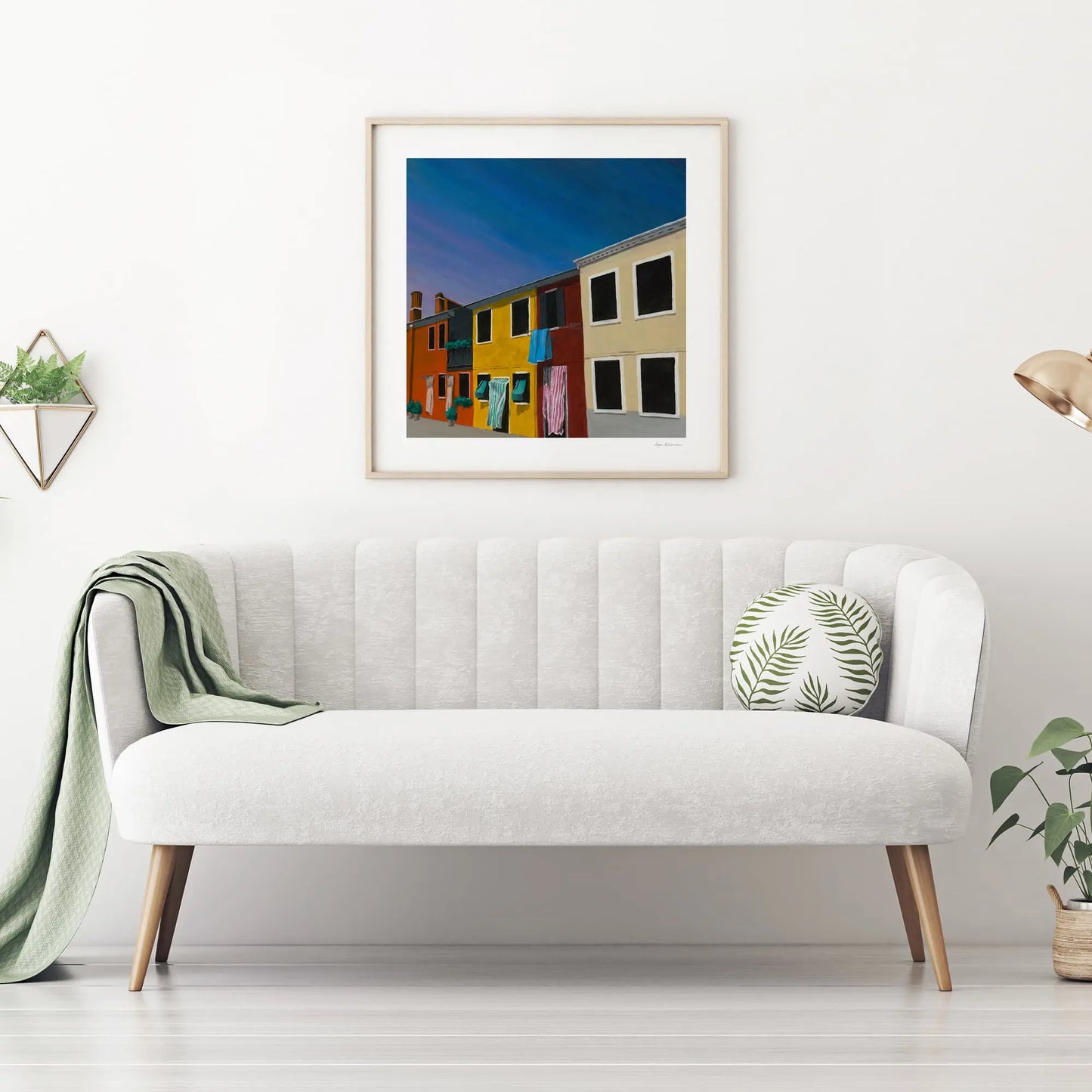 White sofa with a green blanket and pillow in a room with a framed picture on the wall.