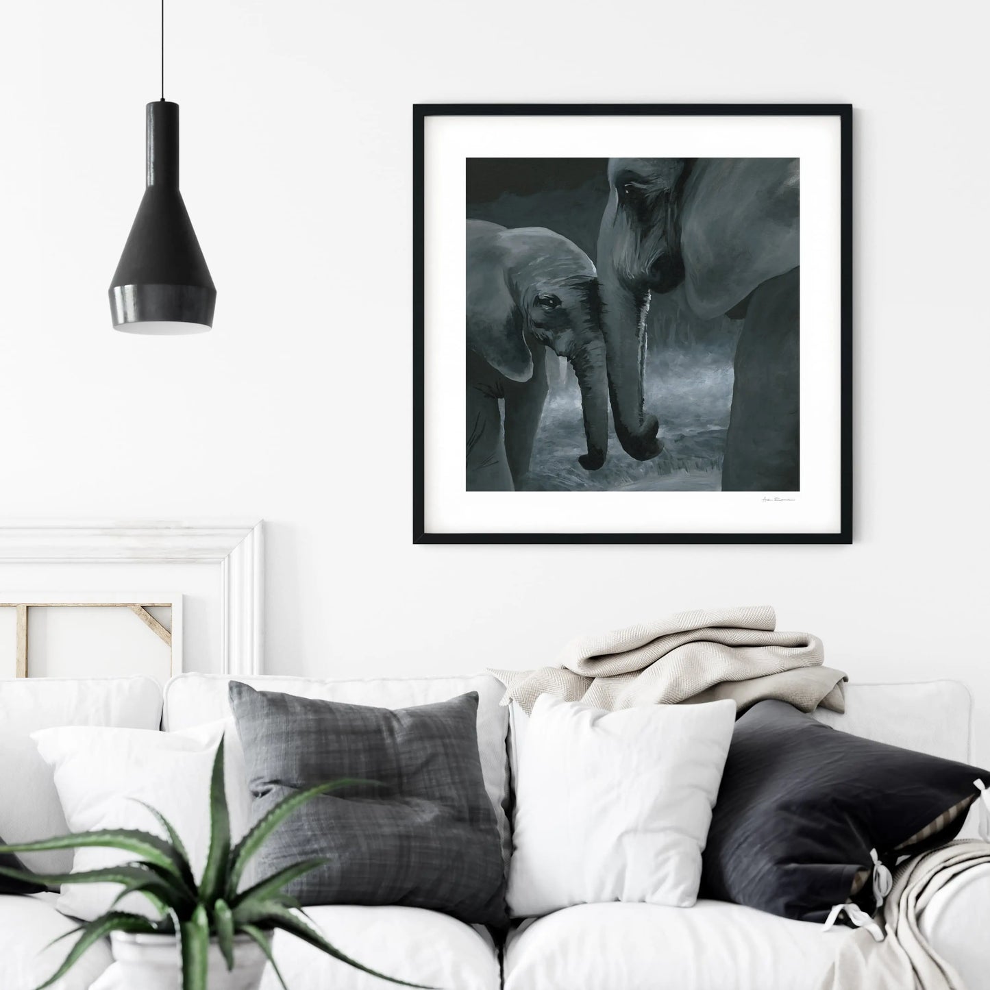 Framed black and white artwork print of two elephants on a wall above a sofa with decorative pillows.