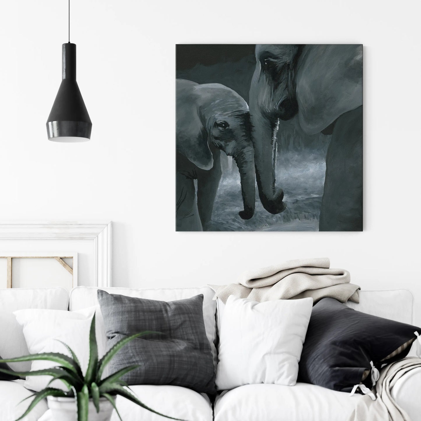 Canvas artwork print of two elephants in a dark setting hanging above a white sofa with decorative pillows.