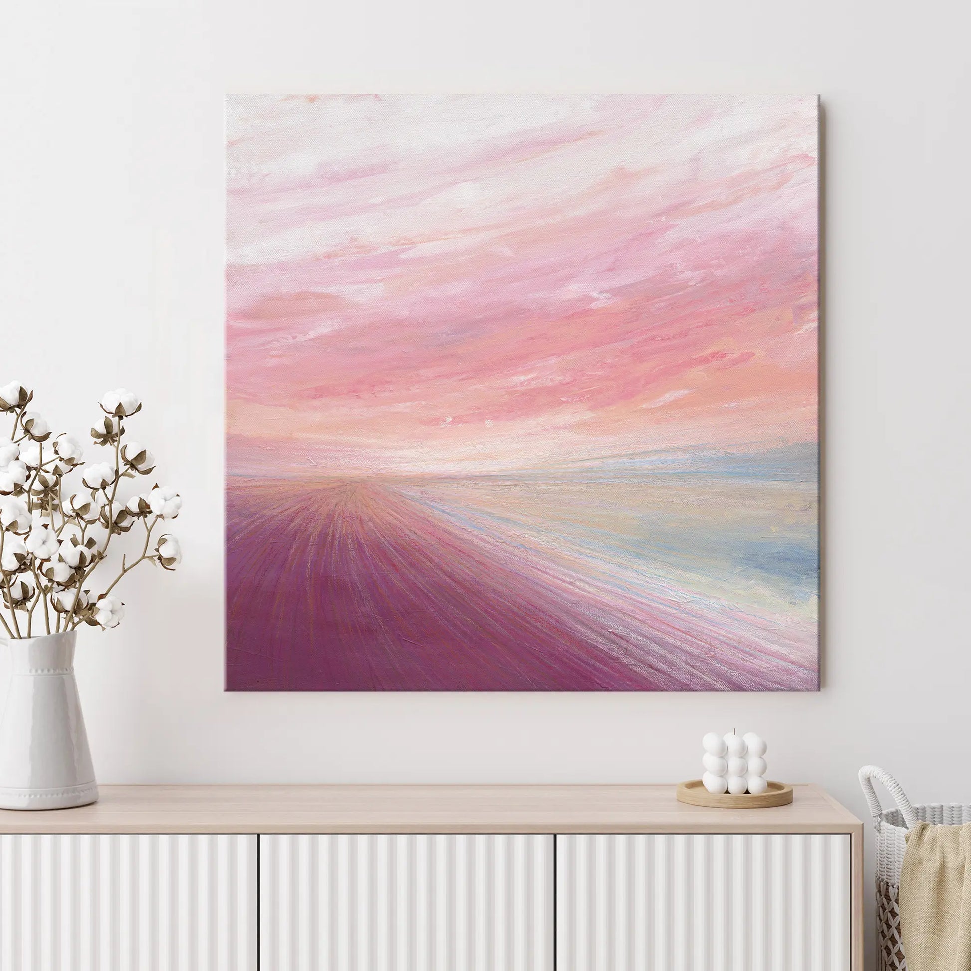 Abstract painting with pink and purple hues on a white wall above a wooden cabinet.