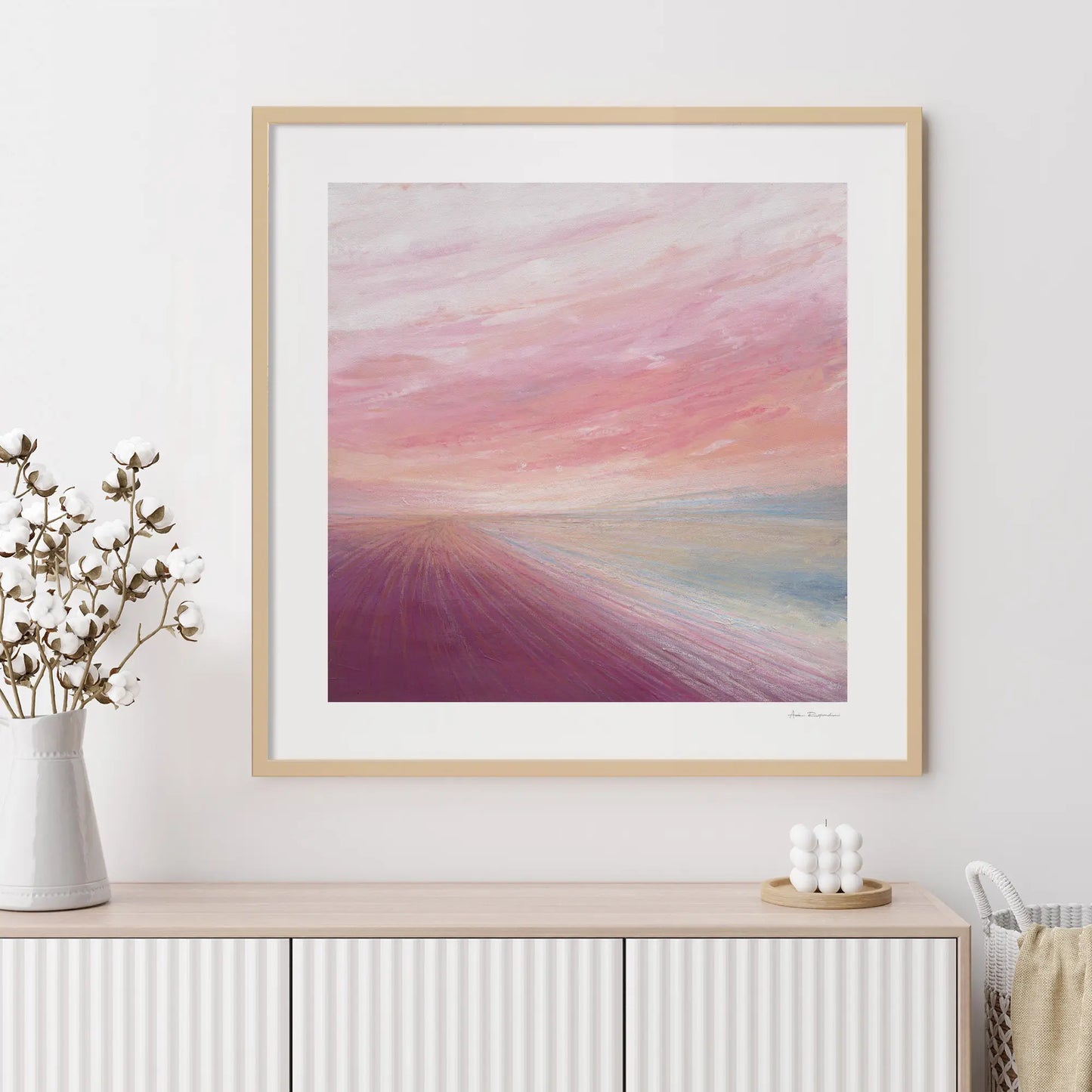 Framed abstract artwork with a colorful gradient on a white wall above a wooden console table.