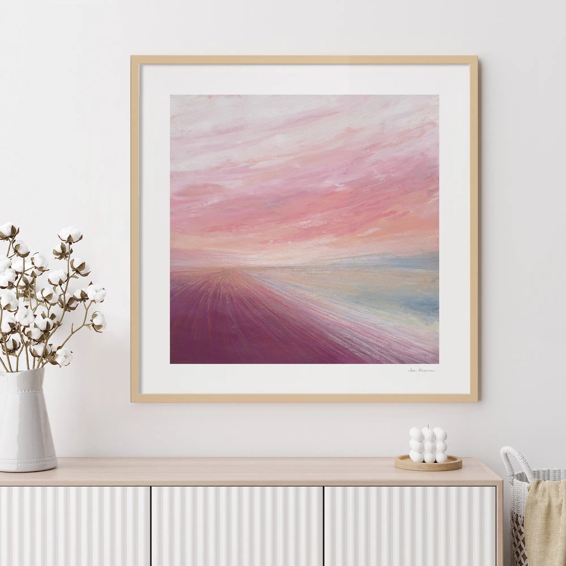 Framed abstract artwork with a colorful gradient on a white wall above a wooden console table.