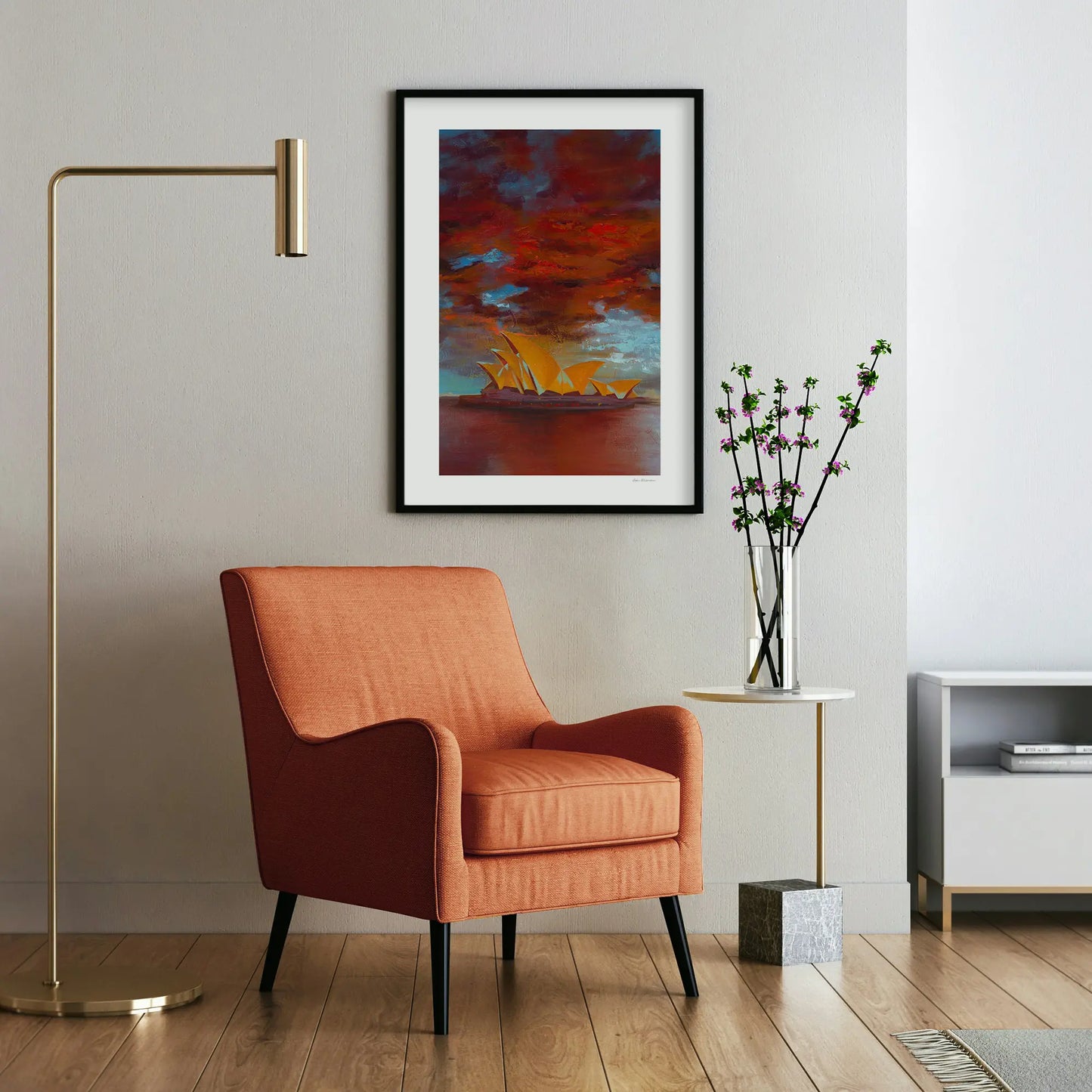 Modern living room with an orange armchair, framed artwork, and a vase with flowers.