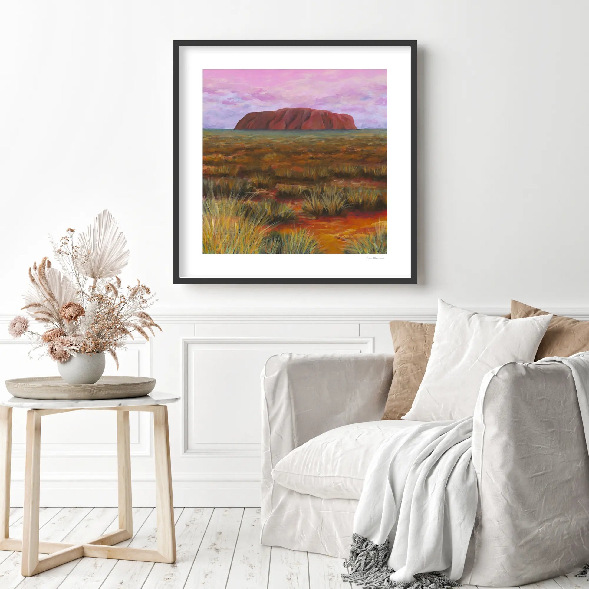 Framed artwork of Uluru in a desert landscape above a sofa in a living room.