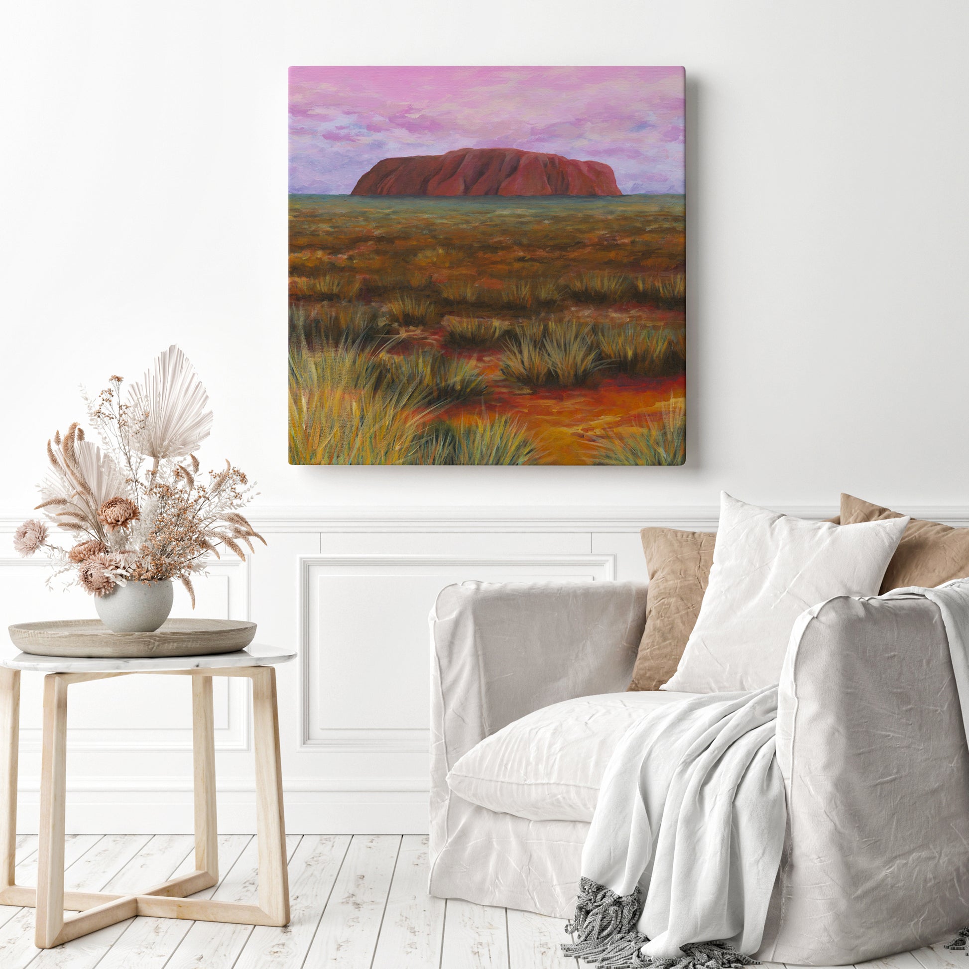 Living room with a painting of Uluru in a desert landscape on the wall, a couch, and a side table with decor.
