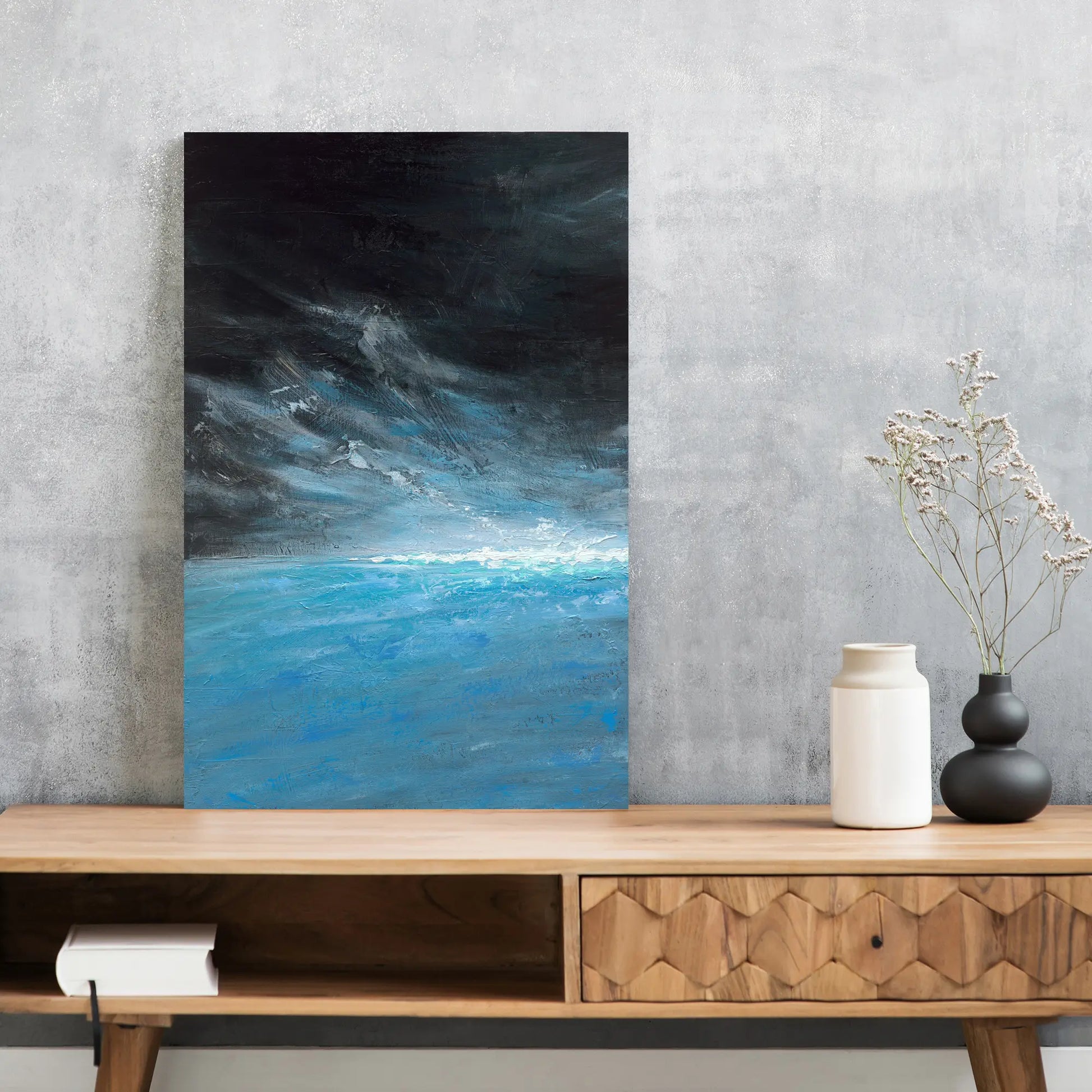 Abstract painting of a blue and black landscape on a wall above a wooden console table with decorative items.
