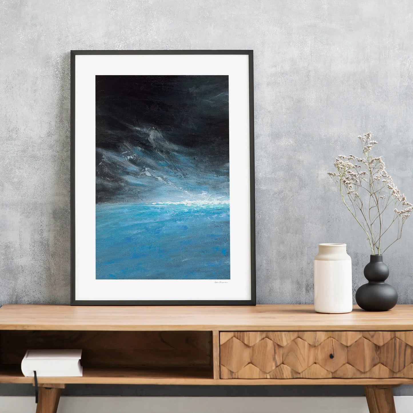 Framed abstract art piece on a wooden console table with decorative vases against a gray wall.