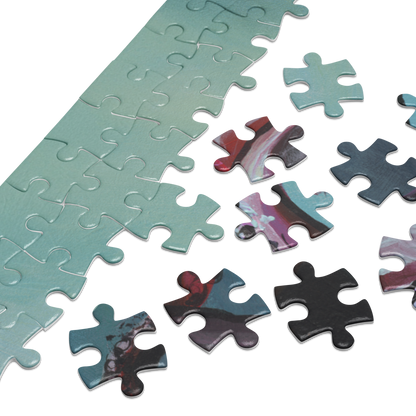 A close-up of a jigsaw puzzle showing a long strip of completed pieces in a pale mint green color, with several loose puzzle pieces beside it featuring a marbled abstract pattern in teal, pink, purple, black, and red on a white background.