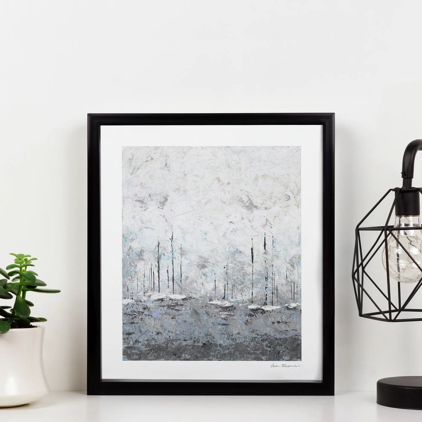Framed abstract art print on a white wall with a plant and lamp in the background