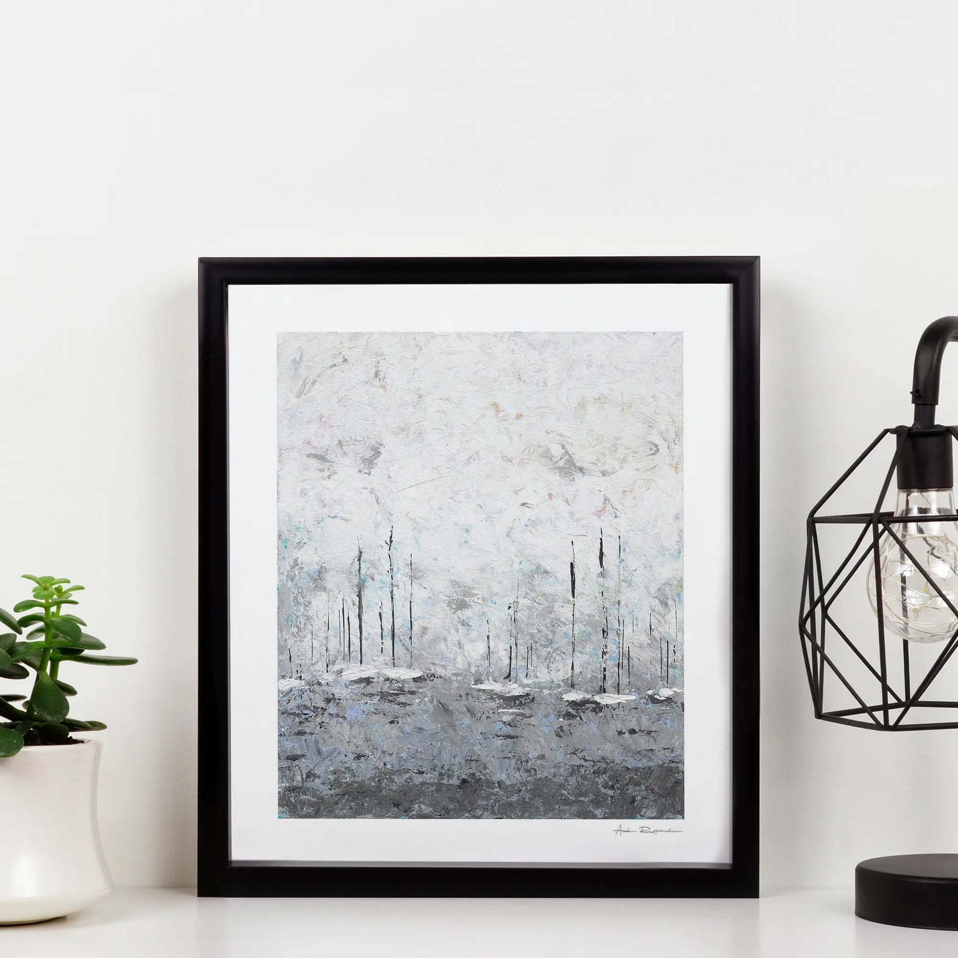 Framed abstract art print on a white wall with a plant and lamp in the background