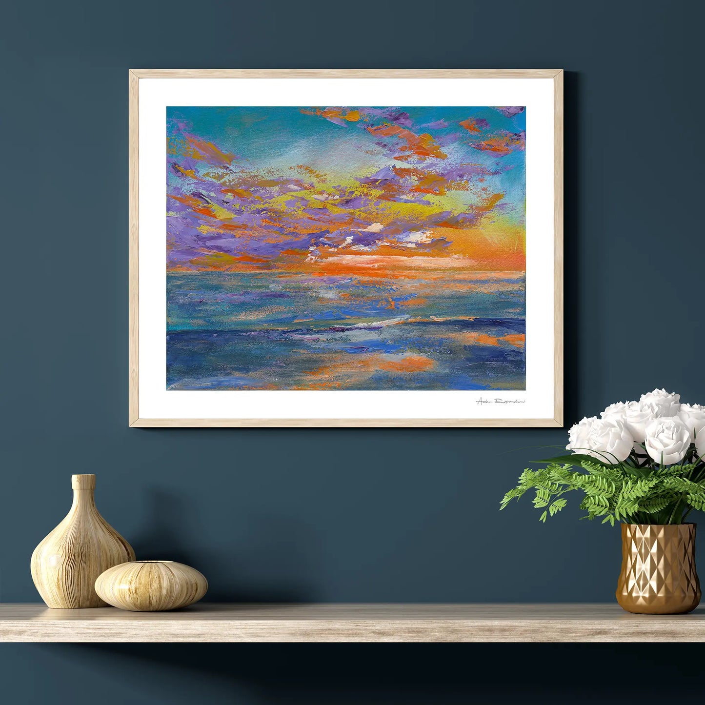 Framed abstract painting of a colorful sky above water on a dark blue wall with decorative items below.